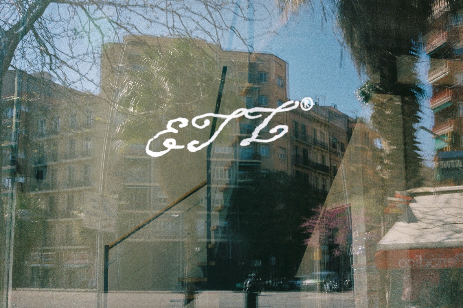 La firma cursiva ETL® dibujada a mano sobre el cristal del local, con el reflejo de los edificios del Eixample detrás.